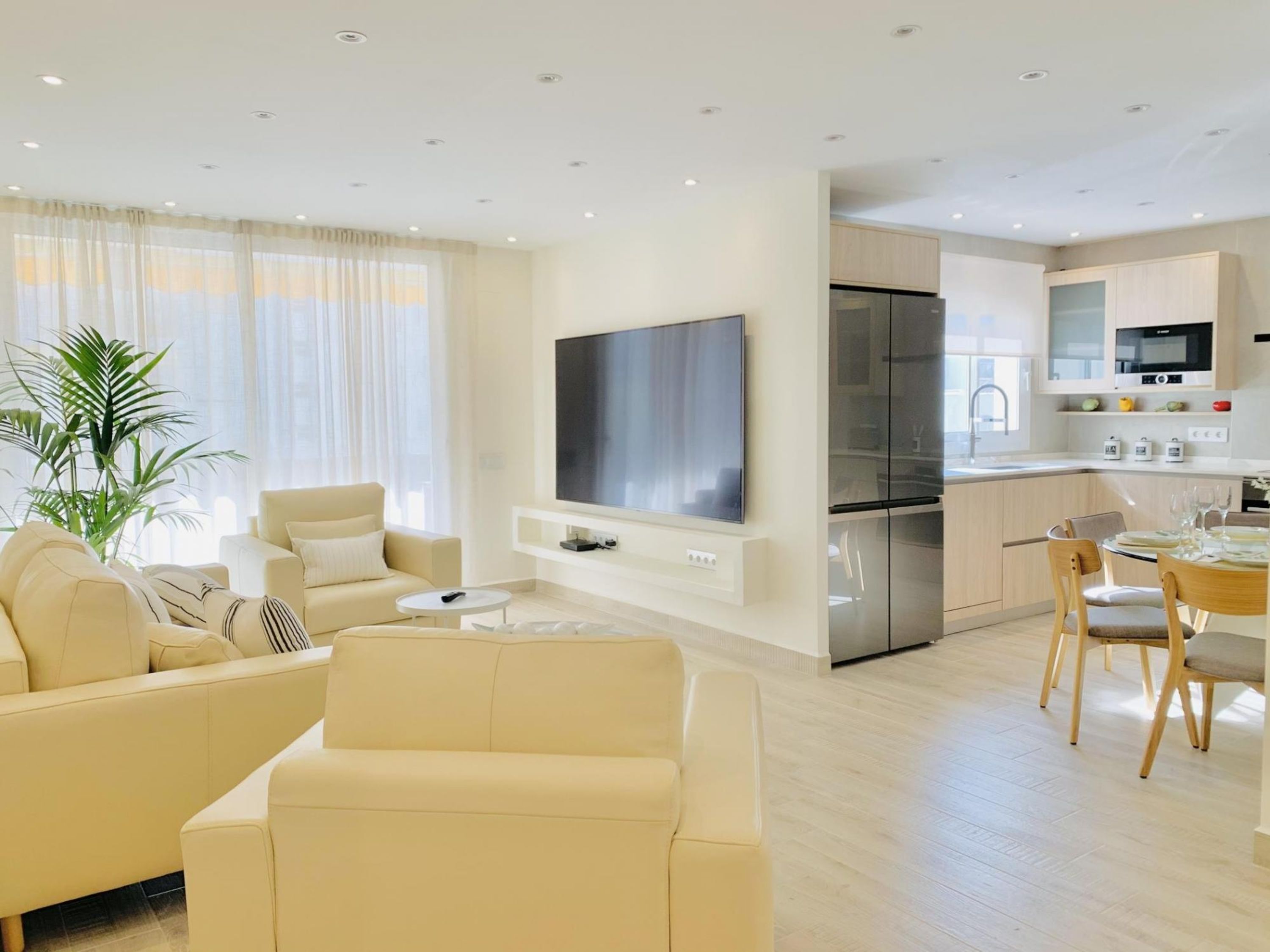 Una sala de estar moderna con sofá, televisor y zona de comedor con sillas y una mesa.