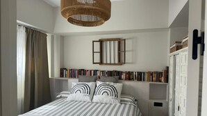 A bedroom with a bed, striped bedding, a bookshelf, a hanging light fixture, and a wardrobe. - Cornelia Suites 03 in Santander (Santander)