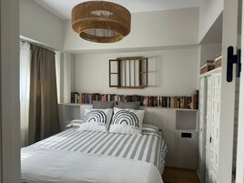 Un dormitorio con cama, ropa de cama a rayas, una estantería, una lámpara colgante y un armario.
