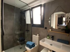 Un baño moderno con cabina de ducha de vidrio, inodoro, lavabo y espejo.