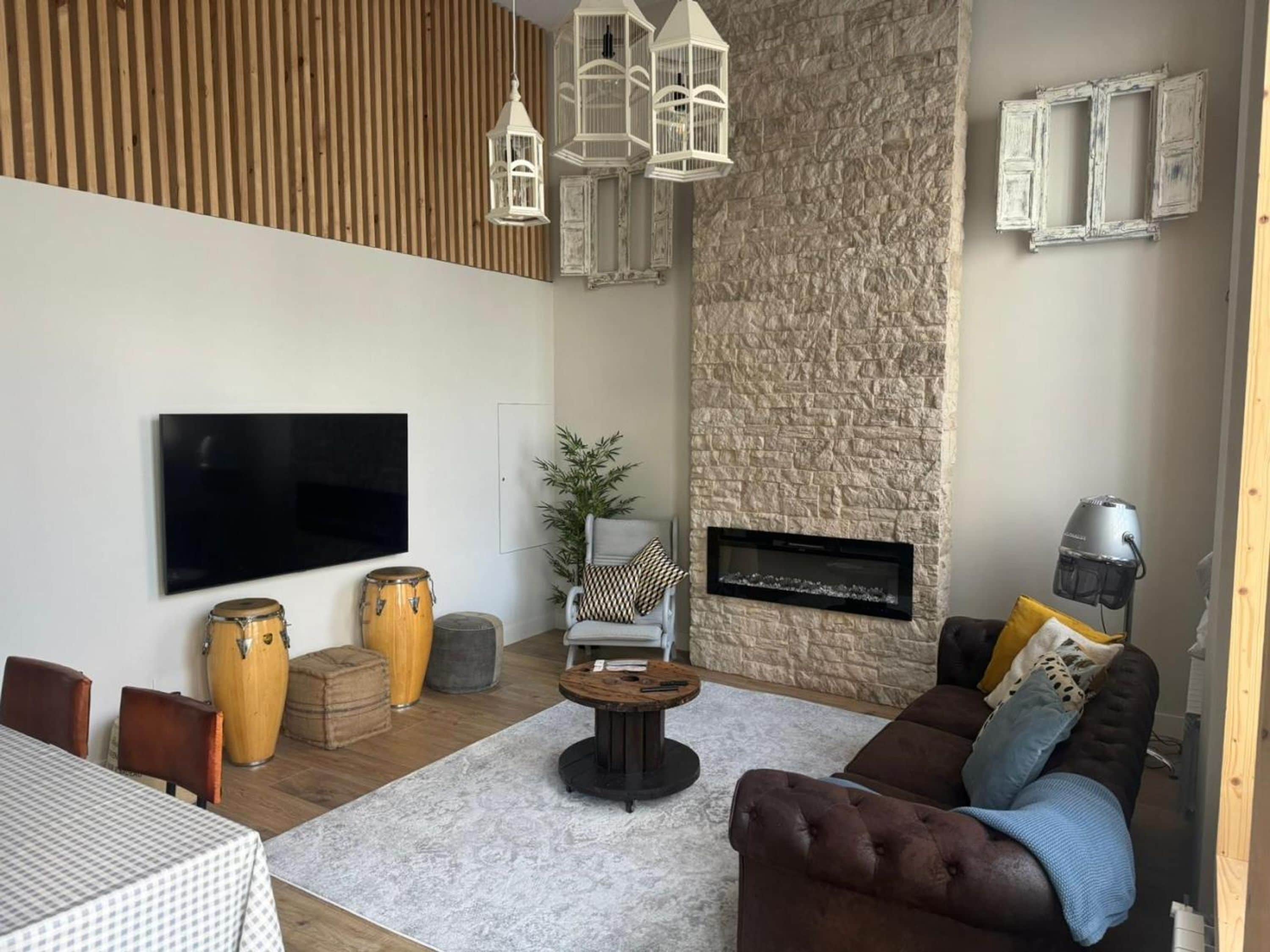 Una sala de estar con pared de piedra, chimenea, televisor y sofá.