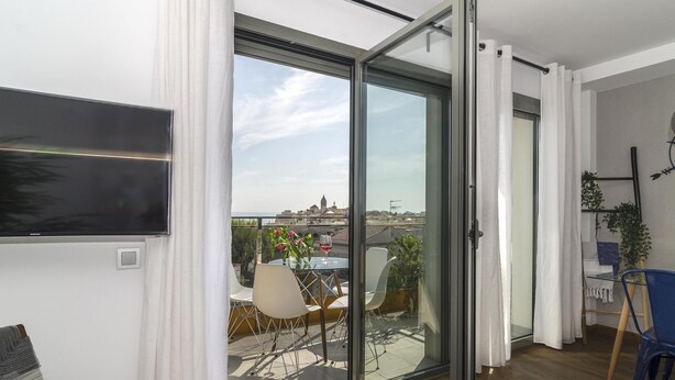 A modern apartment with a sliding glass door leading to a balcony with a city view. - Sitges Spaces Sea View Oasis (Sitges)
