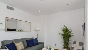 A modern living room with a grey sofa, a small round table, a floor lamp, a potted plant, and a woven chair. - Sitges Spaces Sea View Oasis (Sitges)