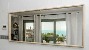 A room with a large mirror reflecting a balcony with a view of the sea and buildings. - Sitges Spaces Sea View Oasis (Sitges)