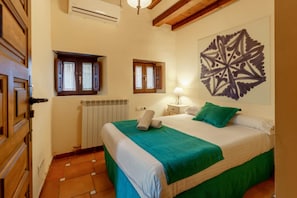 A bedroom with a bed, a radiator, a window, a wall-mounted lamp, and a decorative wall piece.