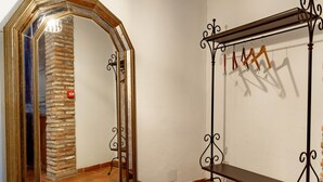 Una habitación con un espejo grande y ornamentado, una percha de metal con ropa y una pared de piedra.