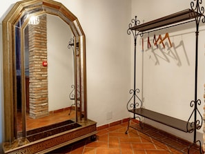 Una habitación con un espejo grande y ornamentado, una percha de metal con ropa y una pared de piedra.