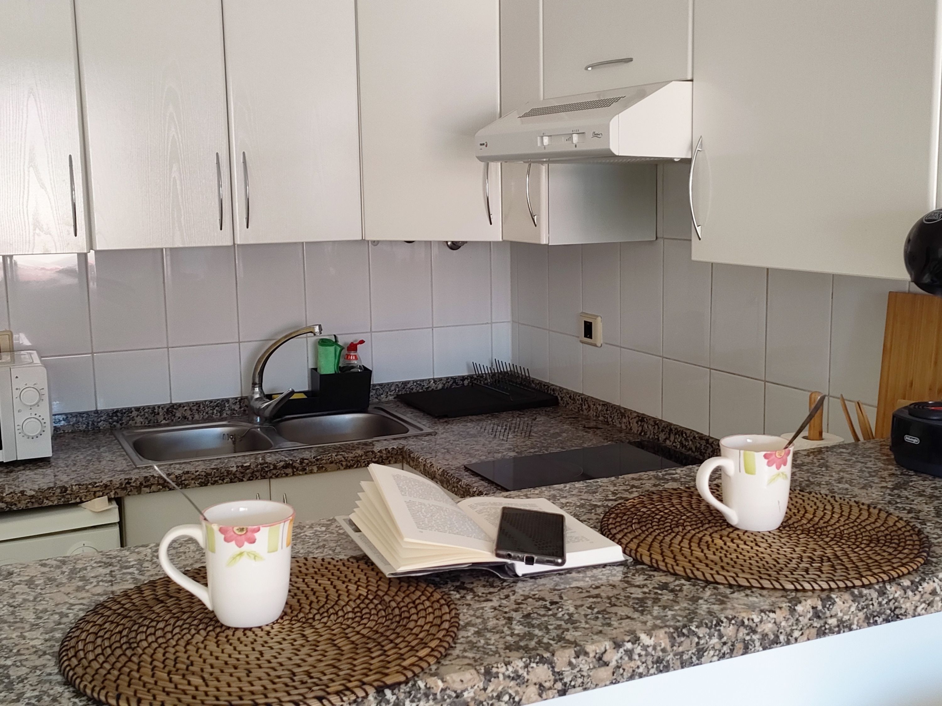 Eine moderne Küche mit weißen Schränken, einer Granit-Arbeitsplatte, einer doppelten Spüle und einer Kaffeemaschine.