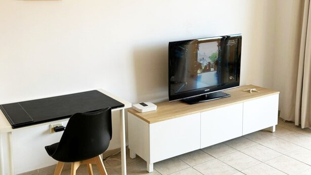 A modern living room with a flat-screen TV, a black chair, a wooden desk, and a framed picture on the wall. - 21 Relax Oasis del mar (Santiago del Teide)