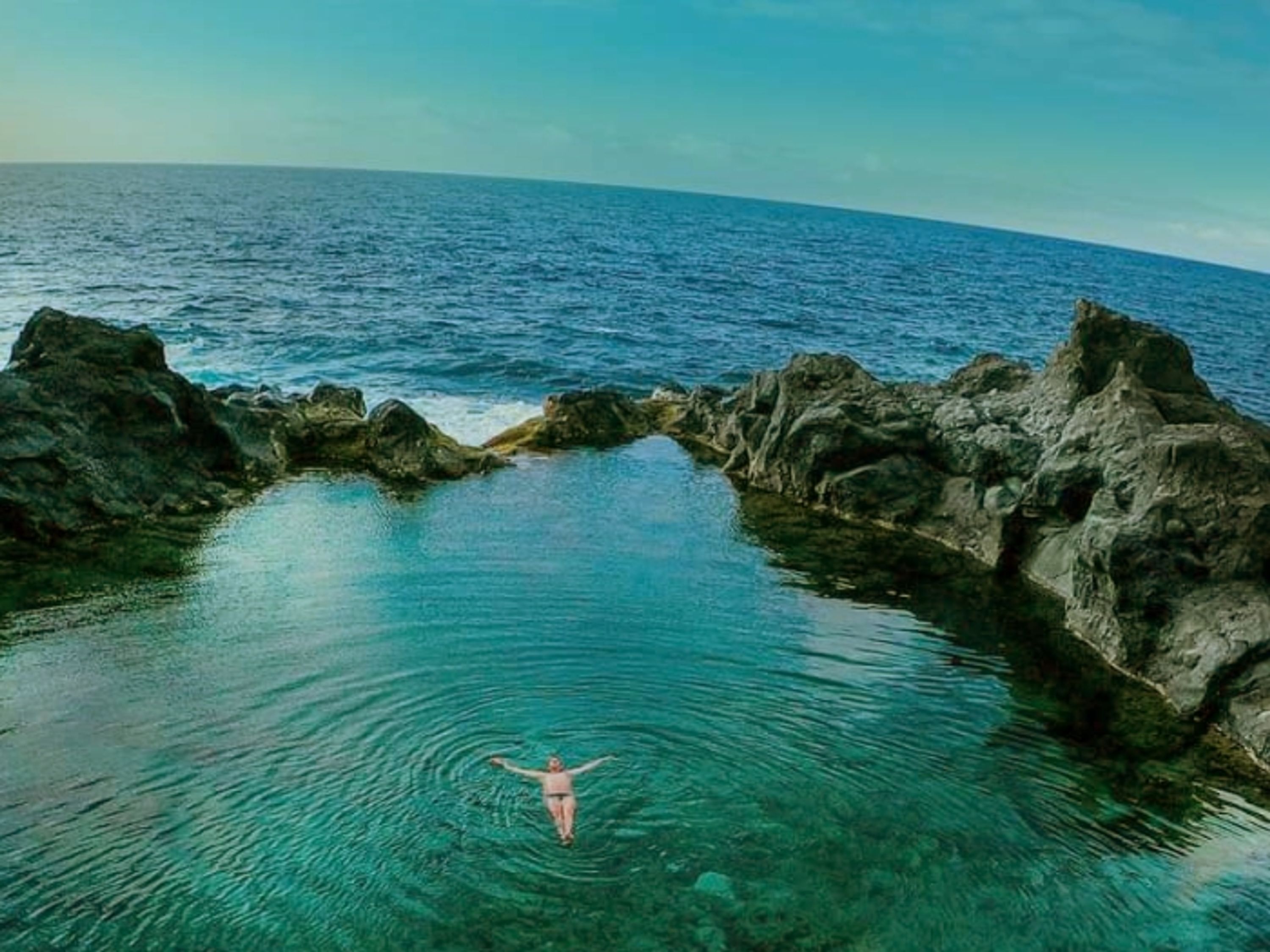 Una persona nada en una piscina natural rodeada de formaciones rocosas.
