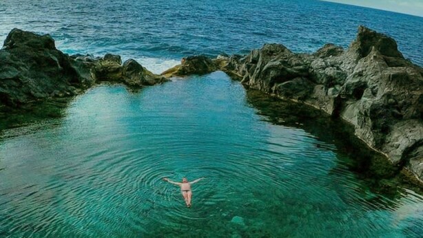 A person swimming in a natural pool surrounded by rocky formations.