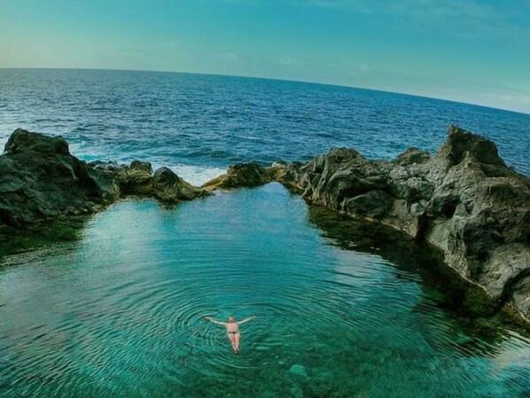 Une personne nage dans une piscine naturelle, entourée de formations rocheuses.