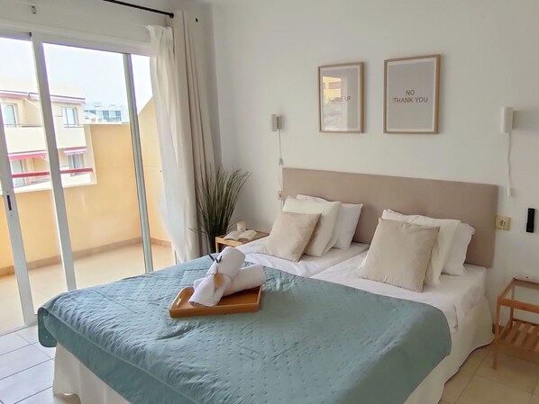 A hotel room with a bed, a bedside table, a nightstand, a potted plant, and a view of the outside. - 21 Relax Oasis del mar (Santiago del Teide)