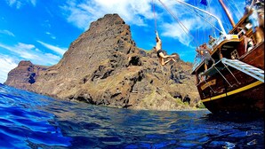 A ship with a person bungee jumping off the bow, a rocky island in the background, and clear blue water.