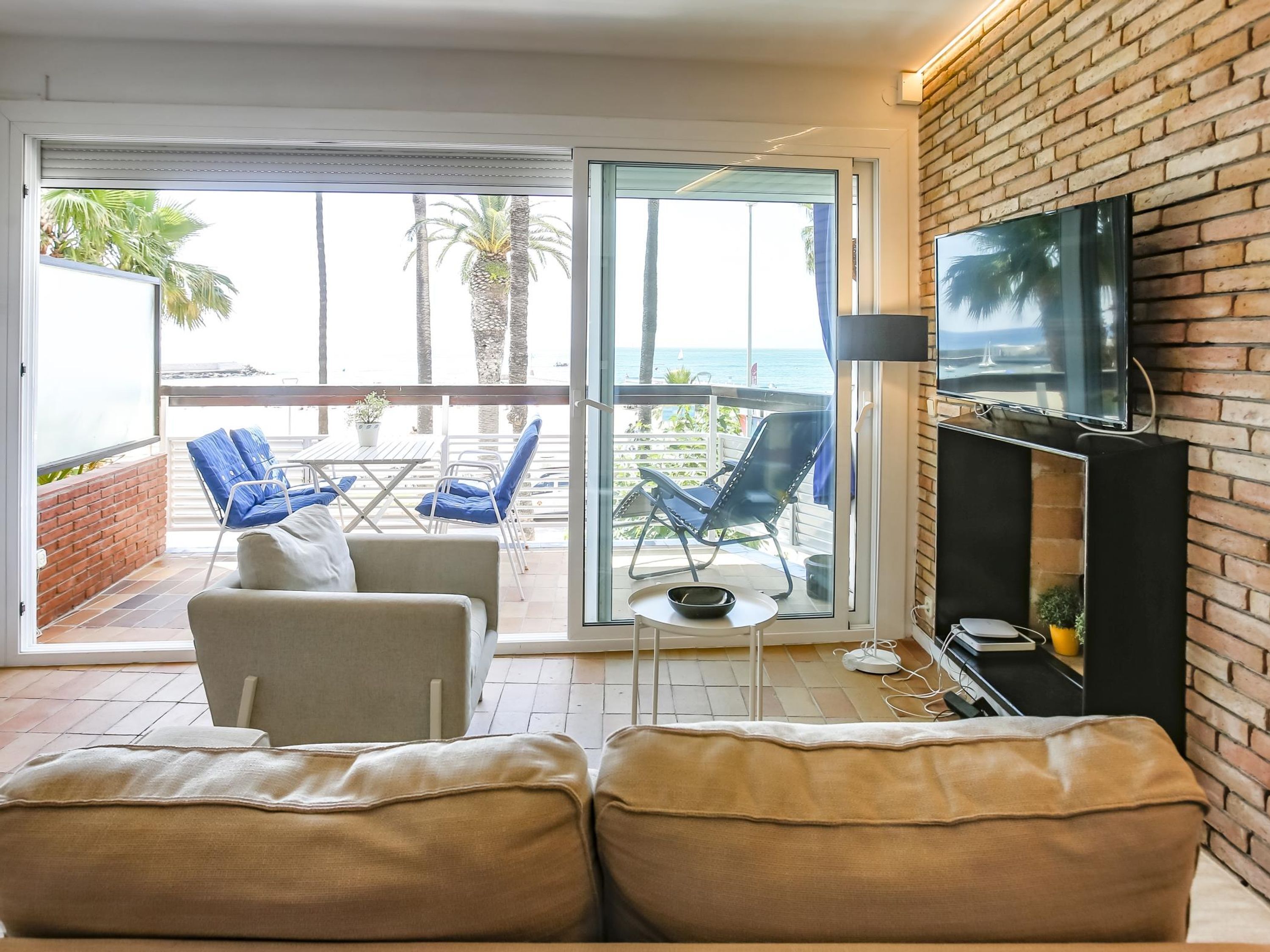 Una sala de estar con sofá, sillas, televisor y balcón con vista al mar.