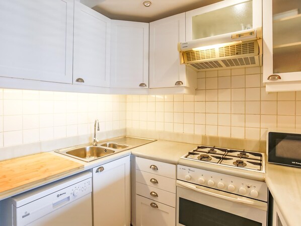 A compact kitchen with white cabinets, a dishwasher, a stove, and a microwave. - Frenta al mar Reci n Reformado Pen Lope (Sitges)