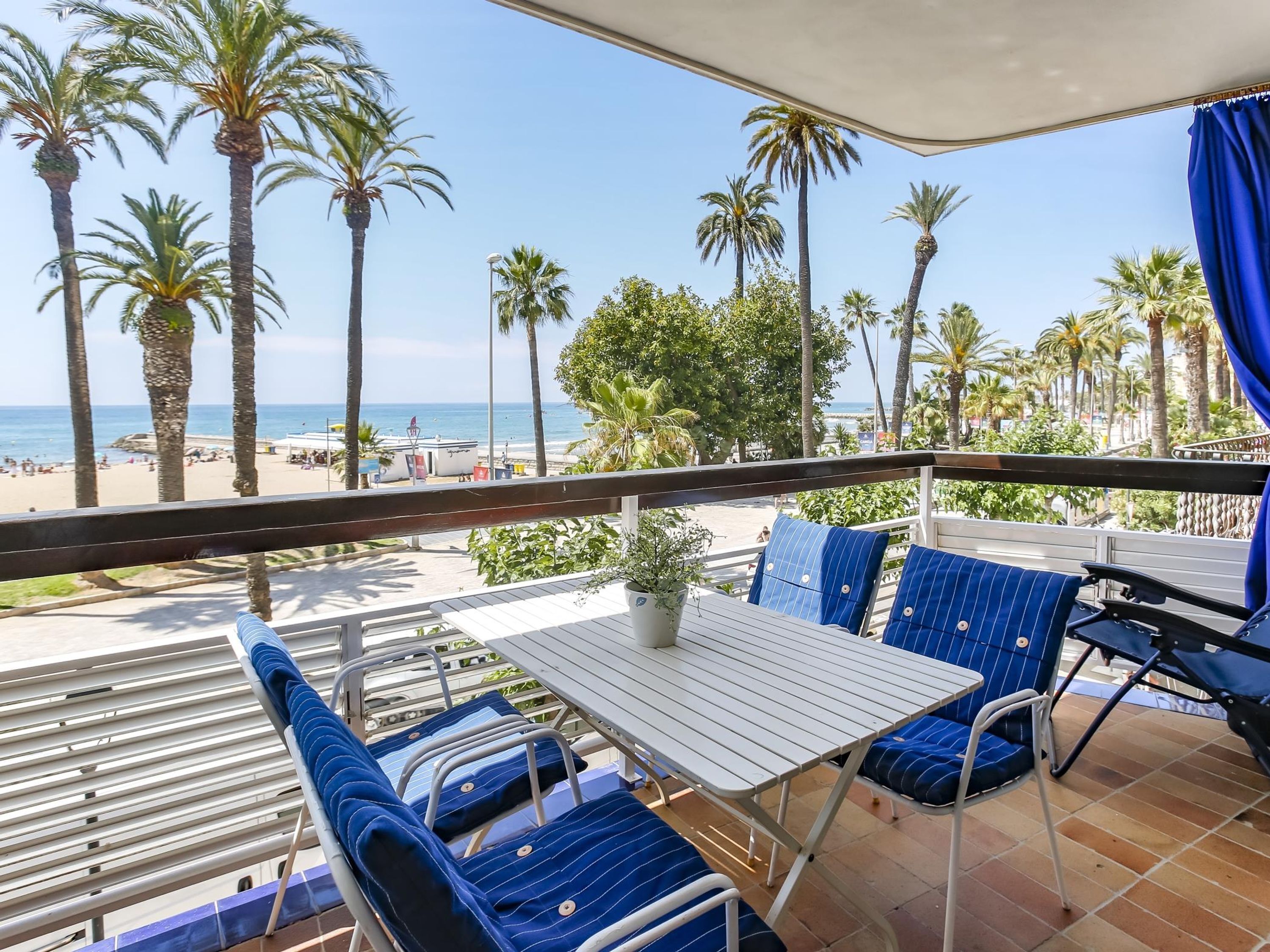 Un balcón con mesa y sillas, con vista a una playa de palmeras y al océano.