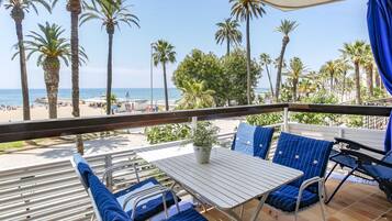 Un balcón con mesa y sillas, con vista a una playa de palmeras y al océano.