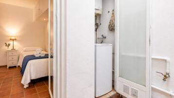 Un dormitorio con cama, mesita de noche, lámpara y baño con ducha.