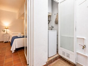 A bedroom with a bed, a nightstand, a lamp, and a bathroom with a shower.