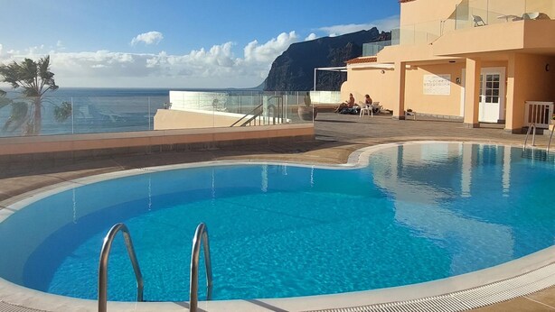 Een zwembad met helderblauw water, een glazen balustrade en uitzicht op zee en bergen.