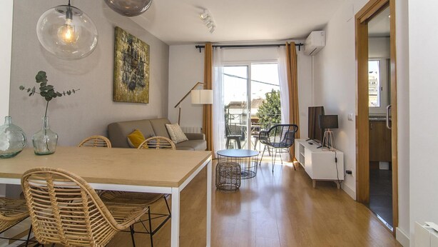 A modern living space with a dining area, a sofa, and a balcony with a view. - Sitges Spaces Terrace Apartment (Sitges)