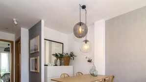 A dining area with a wooden table and wicker chairs, a hanging light fixture, and a mirror above the table. - Sitges Spaces Terrace Apartment (Sitges)
