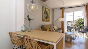 A modern living room with a dining area, featuring a wooden table, wicker chairs, a sofa, and a large window with curtains. - Sitges Spaces Terrace Apartment (Sitges)