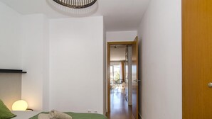 A bedroom with a bed, green bedspread, and a bedside lamp. There is a wooden door leading to a balcony. - Sitges Spaces Terrace Apartment (Sitges)