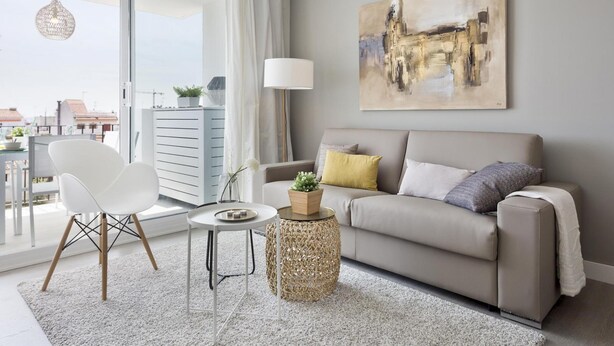 A modern living room with a sofa, a white chair, a small round table, and a large window with a view of buildings.