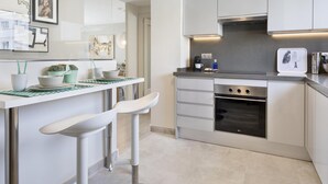 A modern kitchen with white cabinetry, a stainless steel oven, and a countertop with a coffee maker and a potted plant.