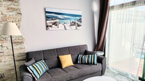 A grey sofa with striped and solid cushions, a white round table, and a beach scene painting on the wall. - Tess Mirador de Ensue o con Vistas Panor Micas (Adeje)
