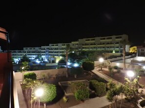A nighttime view of a hotel with multiple floors, illuminated windows, and a landscaped courtyard with various plants. - CM 2 bd Cerca del mar (Granadilla de Abona)