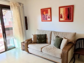 Ein Wohnzimmer mit einem beigefarbenen Sofa, zwei Kissen, einem Holzstuhl und zwei gerahmten Kunstwerken an der Wand.