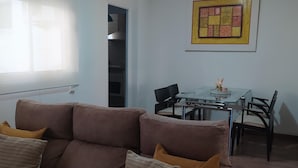 A living room with a brown sofa, a glass dining table with chairs, and a kitchen visible through an open door. - Luminous Flat in Great Location (Valencia)