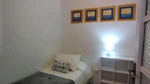 A small, single-bed room with a bedside table, a lamp, and a shelf unit. - Luminous Flat in Great Location (Valencia)