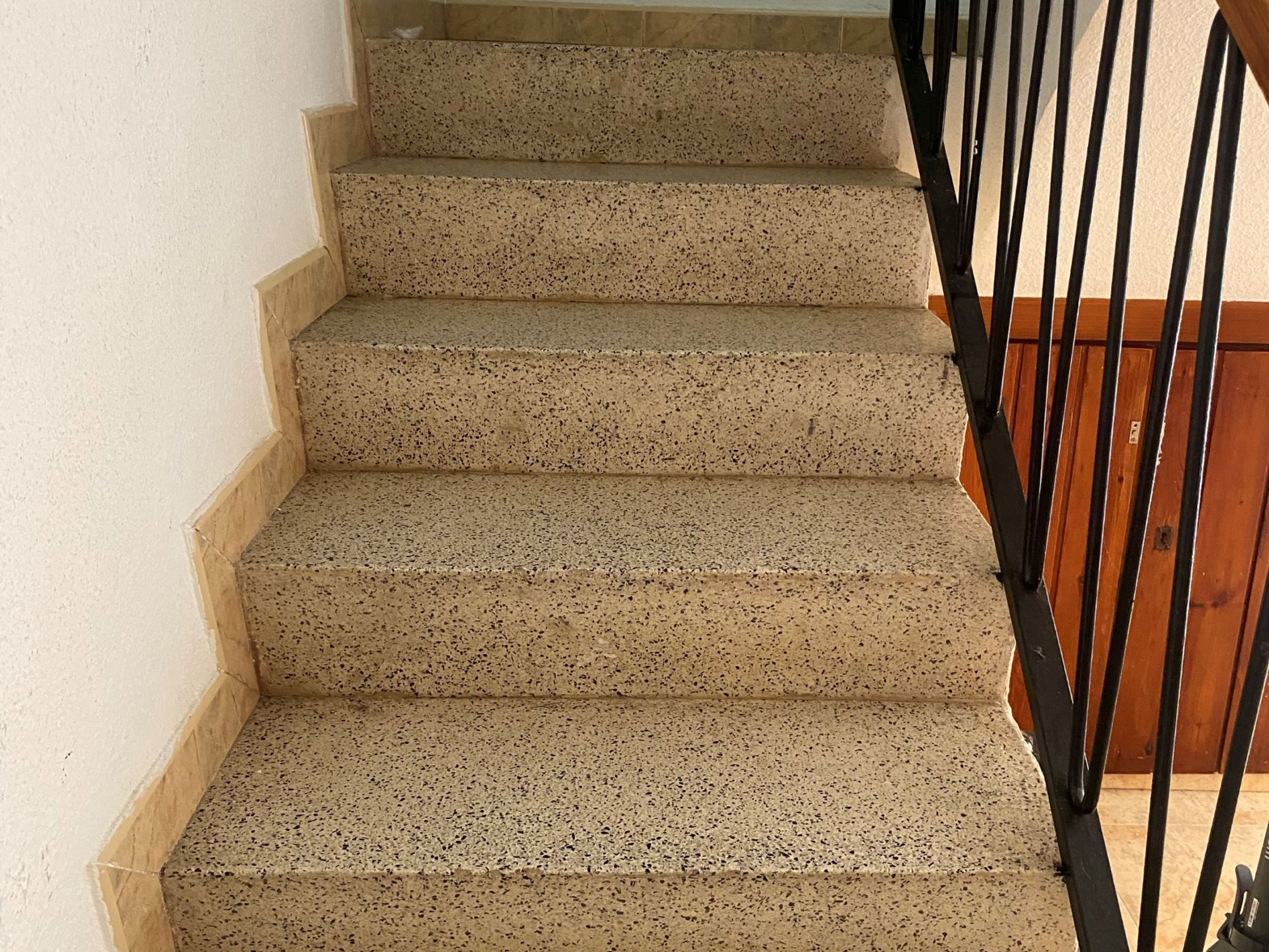 A staircase with speckled beige steps and a black metal railing.
