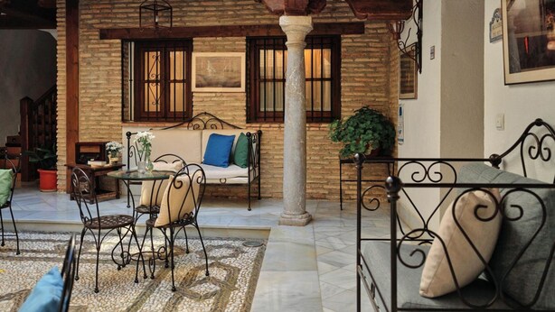 A cozy courtyard with a stone wall, a wooden bench, a metal table, and a metal chair. - Apartamento Fajalauza (Granada)