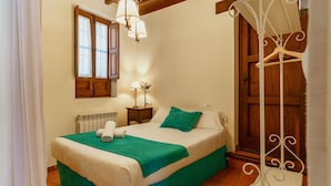 A neatly made bed with a green bedspread and white linens, a bedside table with a lamp, a wooden door, and a window with curtains. - Apartamento Fajalauza (Granada)