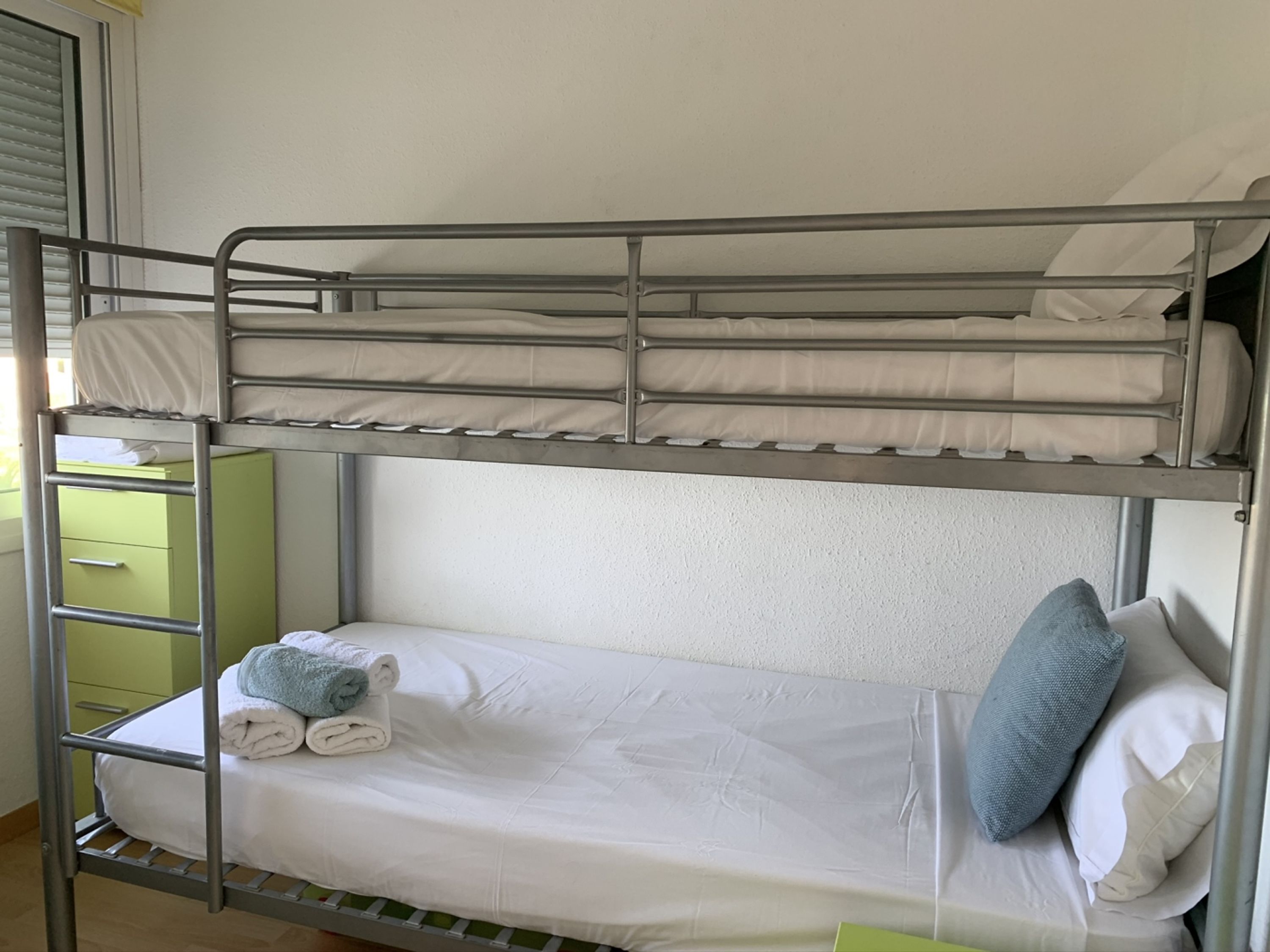 Una cama litera con un armario verde y una escalera.