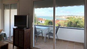 A balcony with a TV on a wooden cabinet, a table, and two chairs. - Ground Floor in Sitges (Sitges)