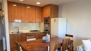 A compact kitchen with wooden cabinets, a gas stove, a microwave, and a white refrigerator. - Ground Floor in Sitges (Sitges)