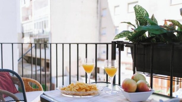 Un balcón con una mesa dispuesta para el desayuno, que incluye un plato de papas fritas, un vaso de jugo de naranja y un bol de fruta.