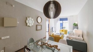 Una sala de estar moderna con una mesa de comedor de vidrio, una lámpara colgante y un sofá.