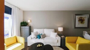 Un salón moderno con un sofá blanco, sillones amarillos, una mesa baja negra y un mueble gris con una planta.