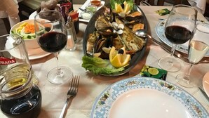 Egy étkezőasztal, melyen tenger gyümölcsei, boros poharak és különféle köretek találhatók.