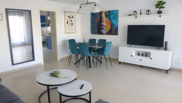 A modern living room with a dining area, a flat-screen TV, and a white entertainment unit.