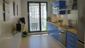 A modern kitchen with blue cabinets, stainless steel appliances, and a large window with blinds.