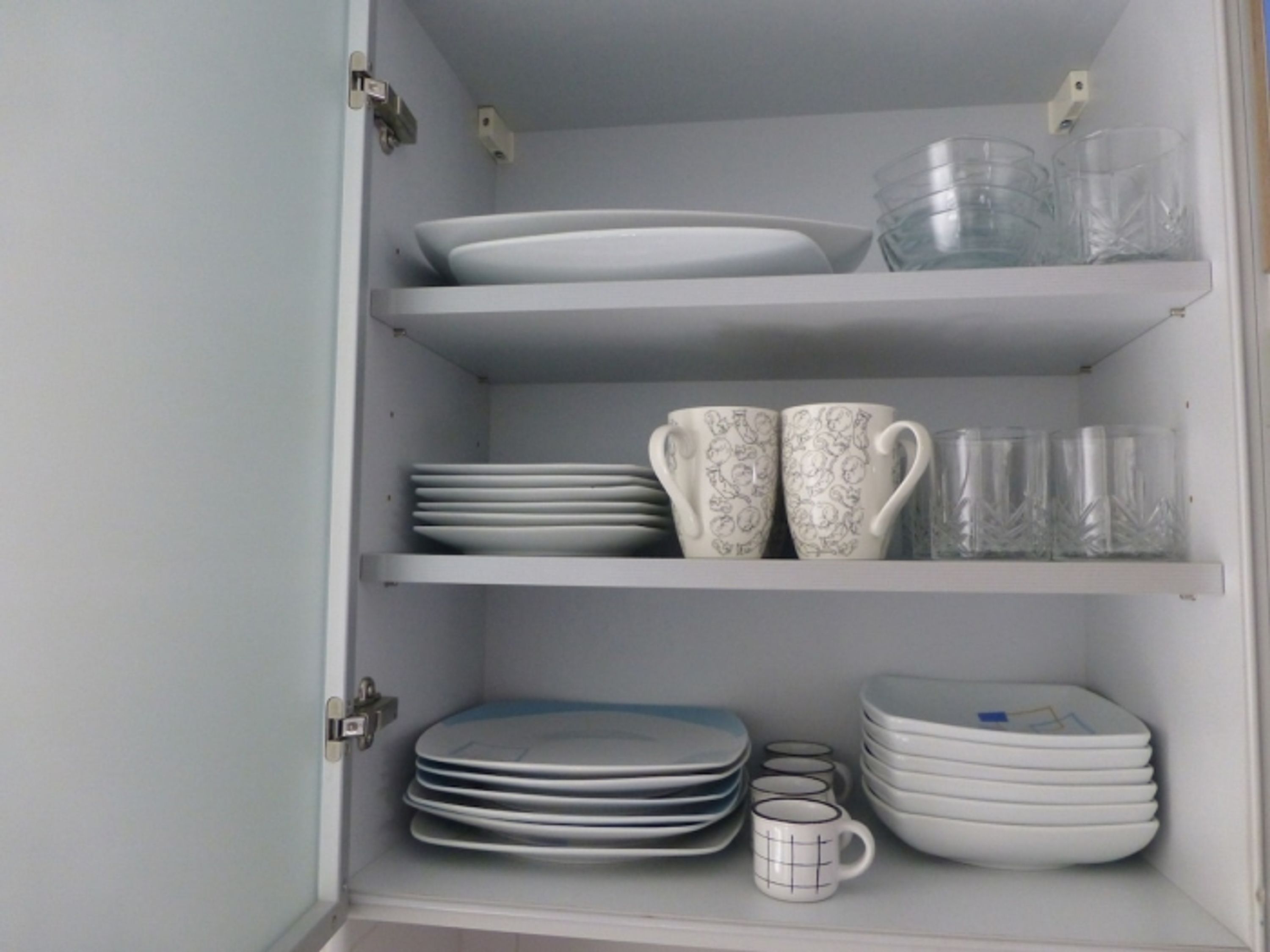 A cabinet with shelves holding plates, bowls, and cups.