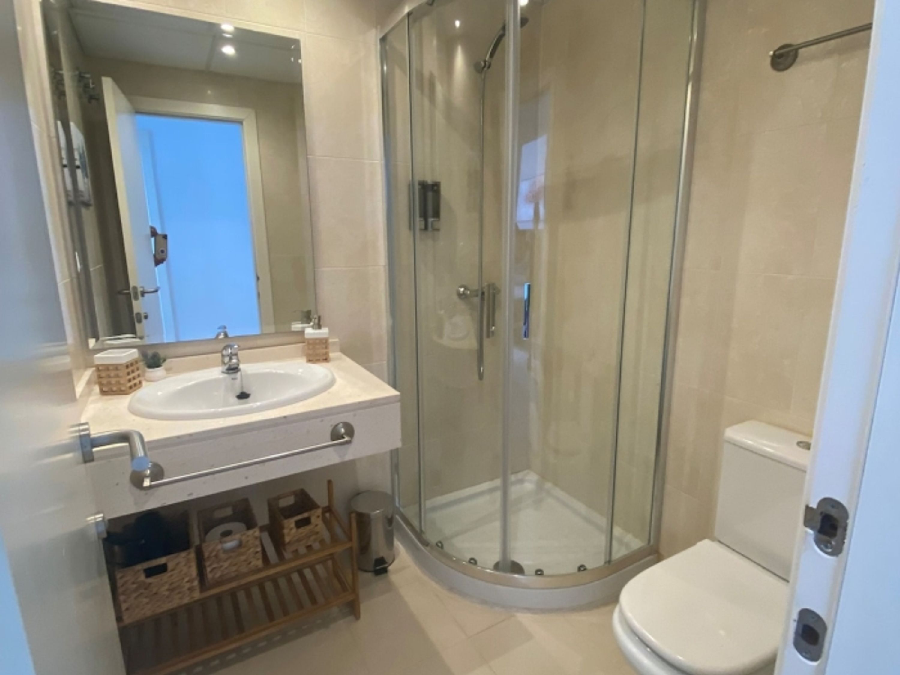 A modern bathroom with a glass-enclosed shower, a sink with a mirror, and a toilet.
